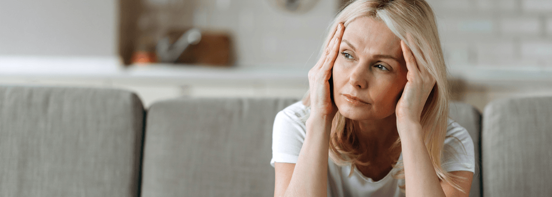 Femme sur un canapé, mains sur la tête, illustrant un moment de stress.